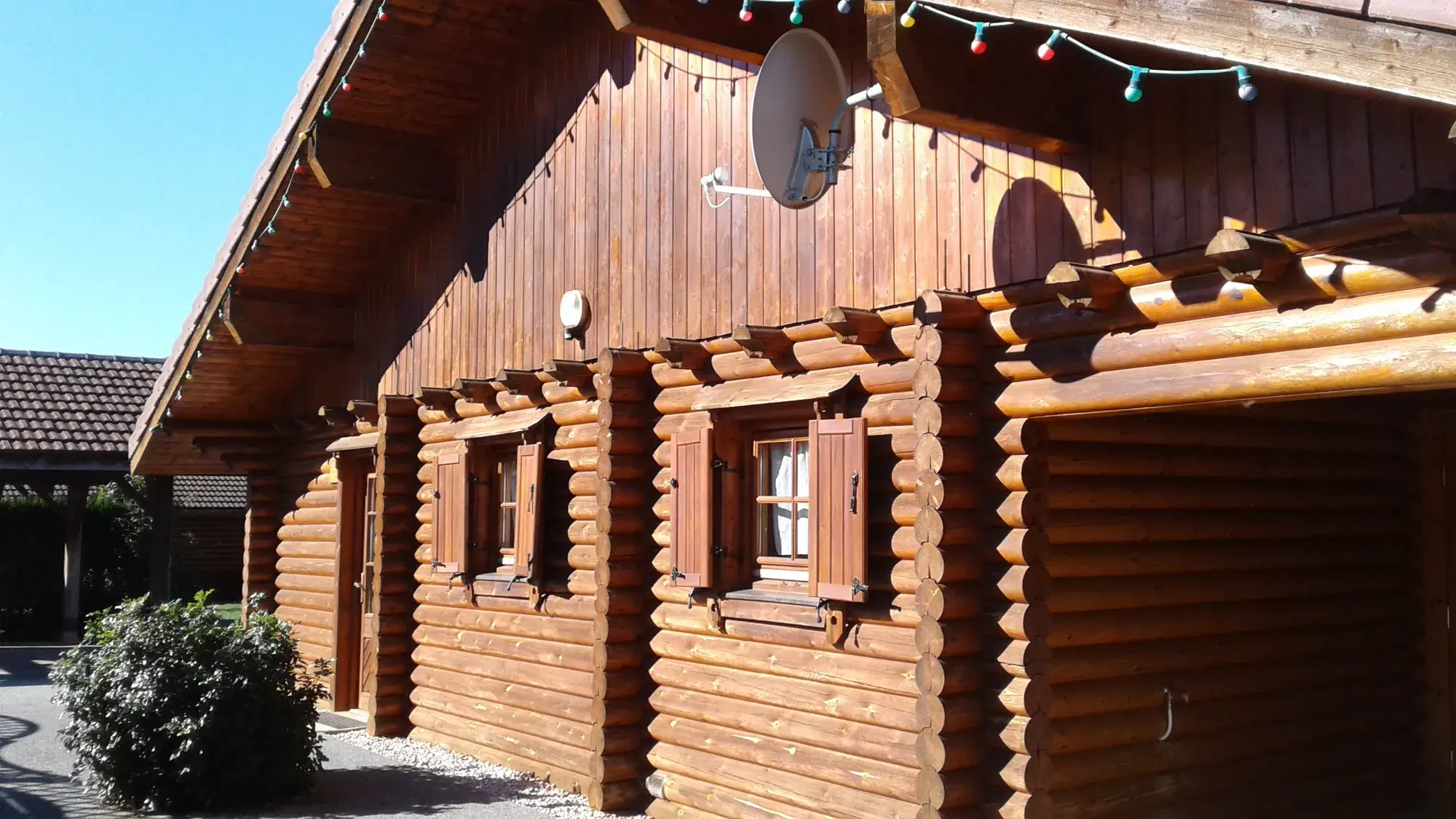 Façade en rondins du Chalet Manon, ses volets en bois et sa guirlande